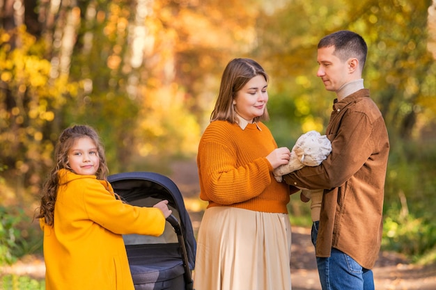 Una felice famiglia tradizionale passeggia nel parco autunnale con i bambini e un passeggino in una giornata di sole