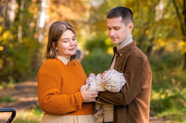 A happy traditional family walks in the autumn park with a newborn baby on a sunny day