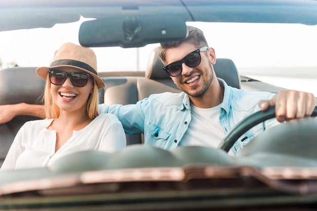 Happy to travel together. Joyful young couple smiling while riding in their convertible