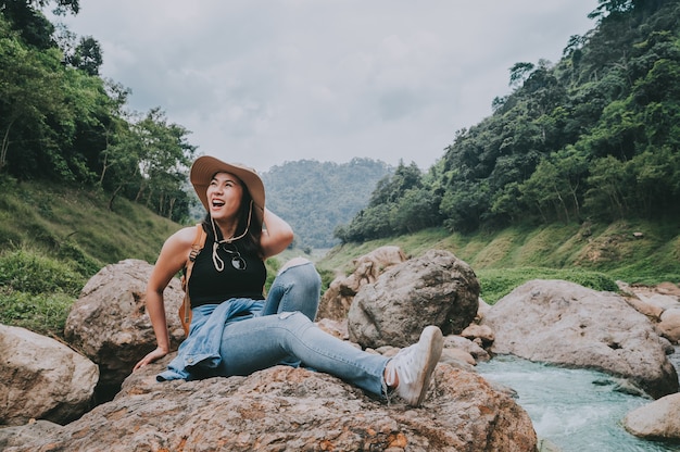 岩の上に座って笑っているバックパックで幸せな旅行者アジアの女性