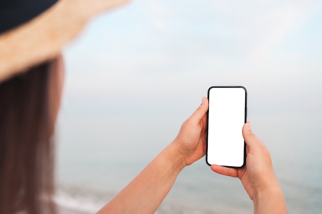 Happy traveler woman in pink dress using mobile phone at tropical beach. Summer, holiday, technology and lifestyle concept. White screen mock up.