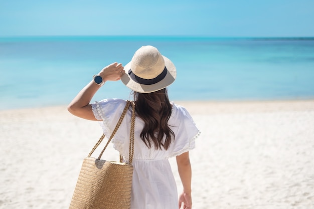 Happy traveler woman in white dress and hat enjoy beautiful sea view