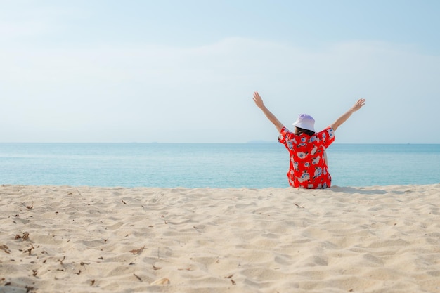 La donna felice del viaggiatore in vestito rosso gode della sua vacanza sulla spiaggia tropicale