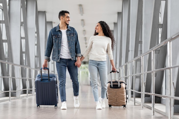 Happy travellers portrait of young arab couple walking with suitcases at airport