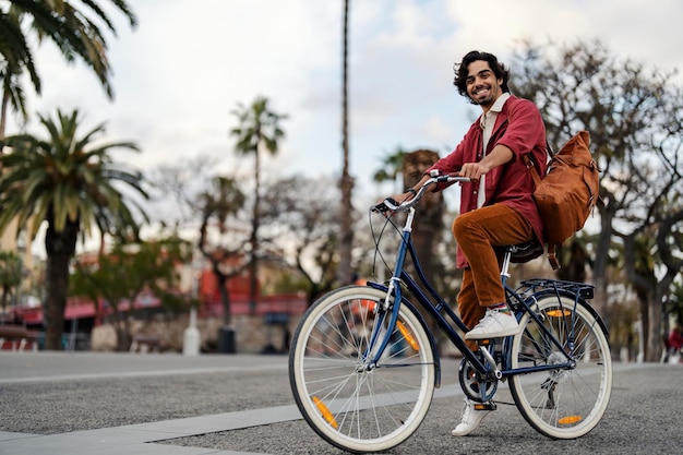 A happy trendy young man is riding a bicycle on city street