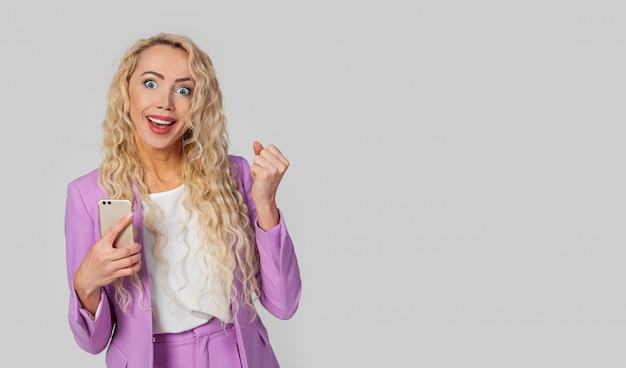 Happy triumphant woman holds a smartphone, fist and an enthusiastic smile, receives great news via text message on a mobile phone