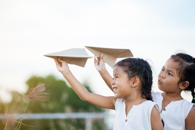 Happy two asian child girls playing with toy paper airplane together in the field 