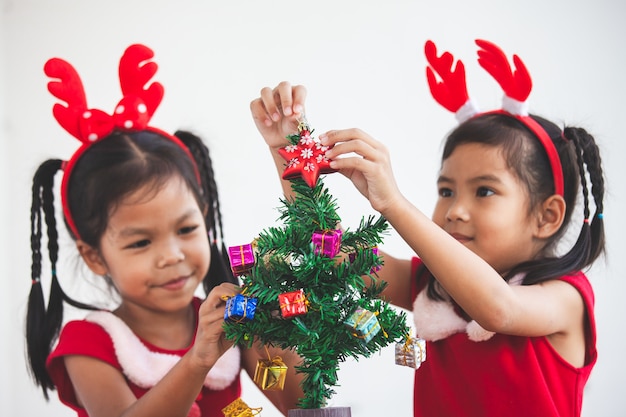 Happy two cute asian child girls decorating Christmas tree for celebrating Christmas