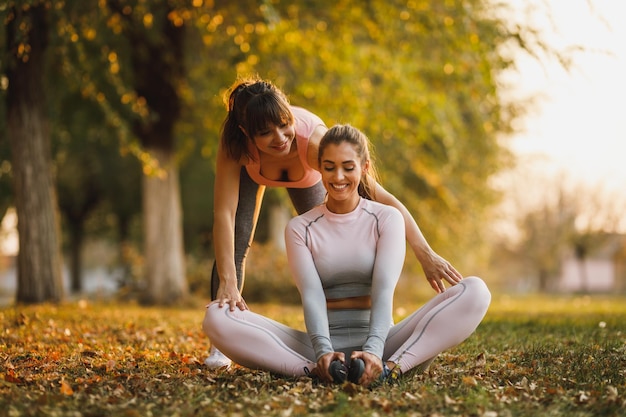 Happy two female friends are doing stretching exercises in nature on a sunny day.