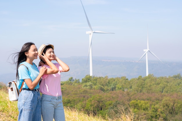 푸른 하늘 Khao Yai Thieng Electric Wind Turbine Thailand와 함께 풍력 터빈과 산을 바라보며 함께 서 있는 행복한 두 소녀