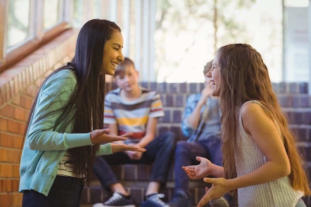 Photo happy two schoolgirls interacting with each other in corridor