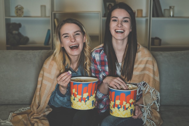 Le due donne felici con un popcorn guardano un film sul divano
