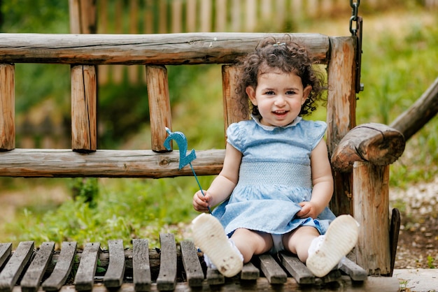 Foto felice bambina di due anni seduta sulla panchina e con in mano la candela del suo numero di compleanno