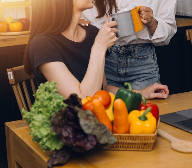 사진 행복한 두 젊은 여성이 집 부엌에서 함께 요리하는 동안 노트북 컴퓨터를 보고 있습니다. lgbt와 성 정체성 개념을 함께 시간을 보내는 두 젊은 다양한 레즈비언 여성