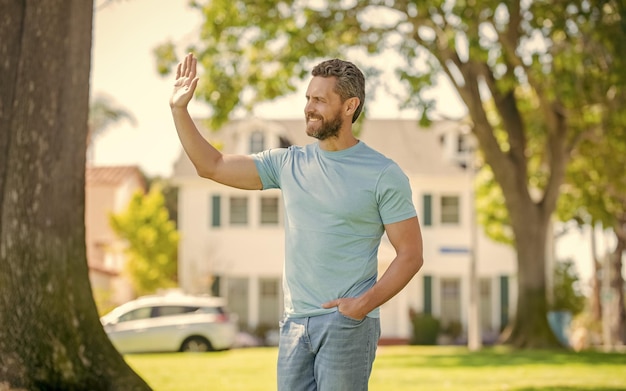 Happy unshaven guy welcoming visitors near new house welcome