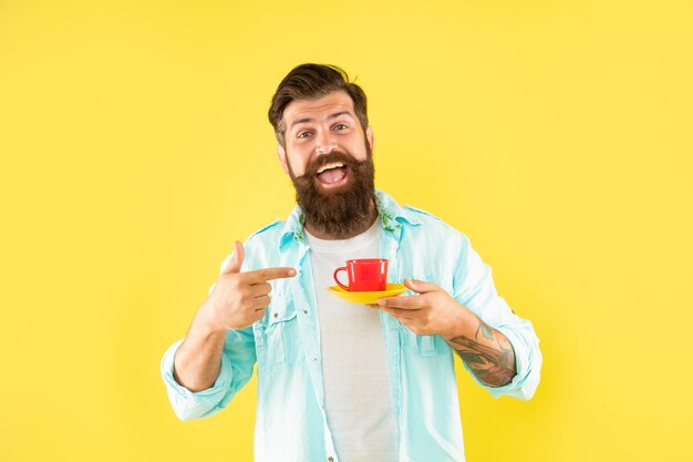 Happy unshaven man in shirt point finger on coffee on yellow backdrop coffee