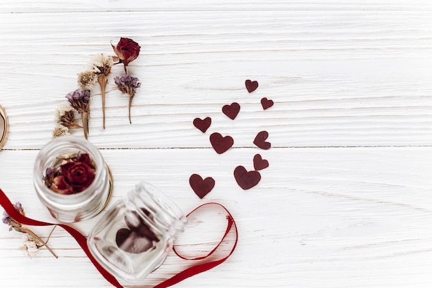 Foto felice giorno di san valentino cuori alla moda in vaso di vetro e rose e nastri su fondo di legno bianco biglietto di auguri insolito piatto giaceva con spazio per il testo