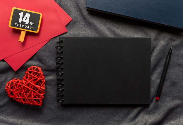 С Днем Святого Валентина концепция, черная книга, красное сердце и ручка на серой ткани