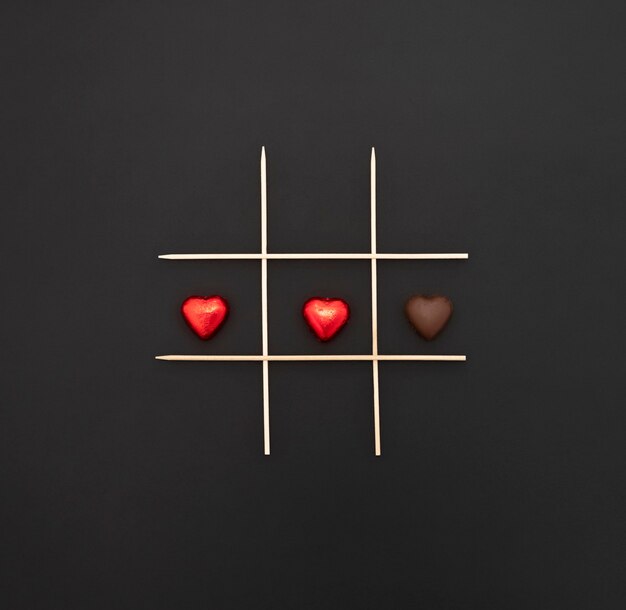 Foto buon san valentino. gioco di tris con cuori di cioccolato con e senza incarto. parete nera e iscrizione in gesso.