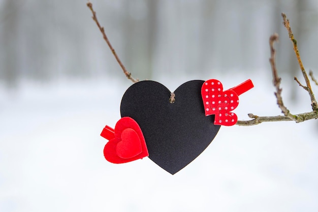 Happy Valentine's Day greeting card or banner. Red hearts on a branch of a snow-covered tree in winter. Holidays Happy Valentine's Day. Snowfall on the background of the forest