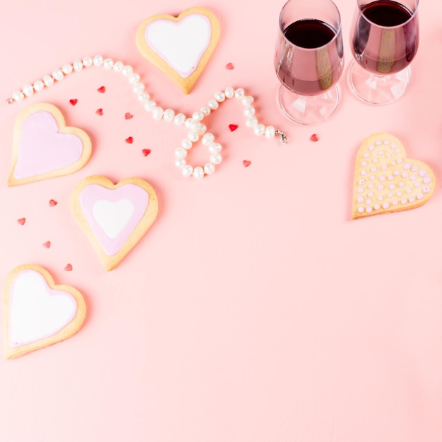 Happy Valentine's day greeting card with heart cookies, wine glasses and wine on pastel pink background.