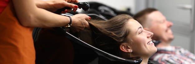 Happy visitor to beauty salon lie with her head in black washbasin