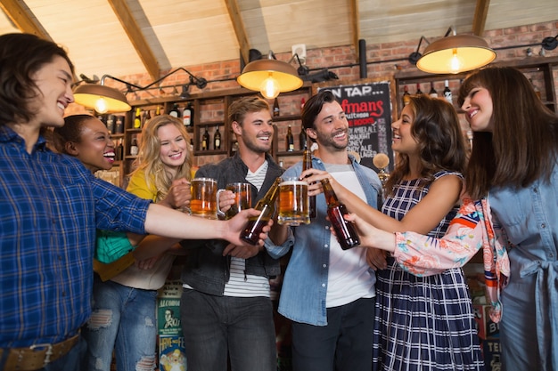 Happy vrienden roosteren bierglazen en flessen in de pub