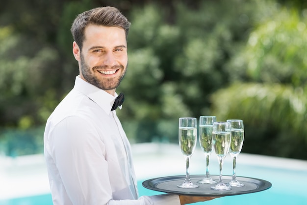 Happy waiter carrying champagne flutes on tray 