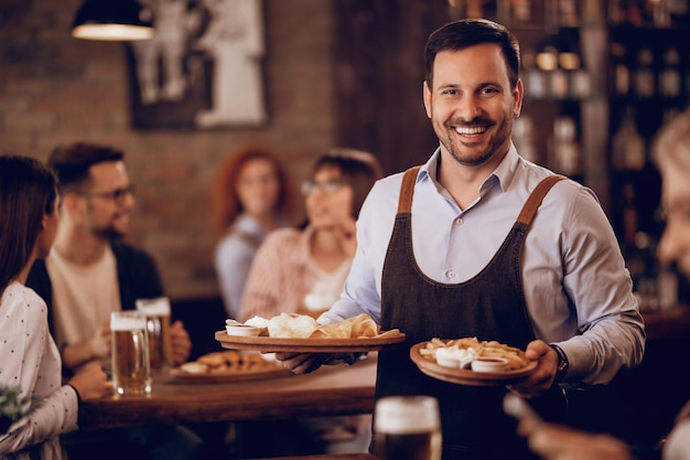Happy waiter serving food and looking at camera in a tavern