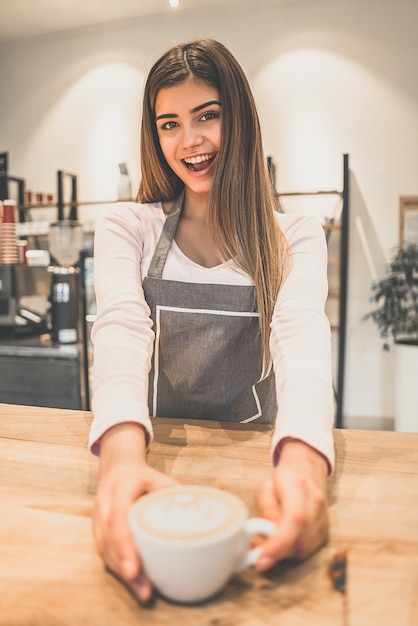 Photo the happy waitress holding a cup of coffee in a cafe