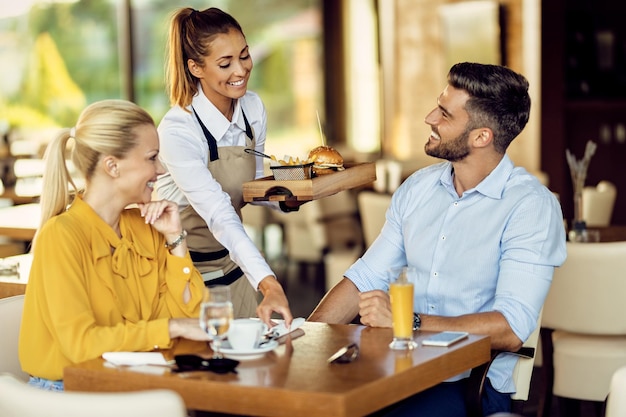 レストランでカップルに食事を提供する幸せなウェイトレス