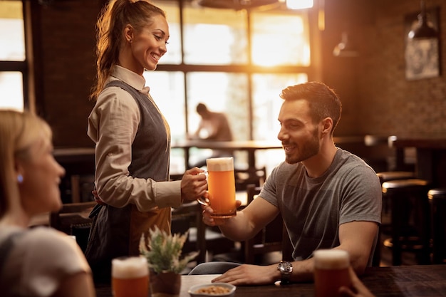 Happy waitress serving male guest with lager beer in a pub