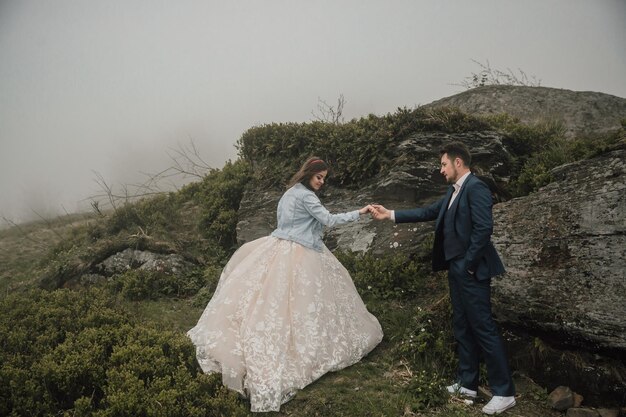 Happy wedding couple in the mountains near a big stone holding hands Wedding photo session in nature Photo session in the forest of the bride and groom