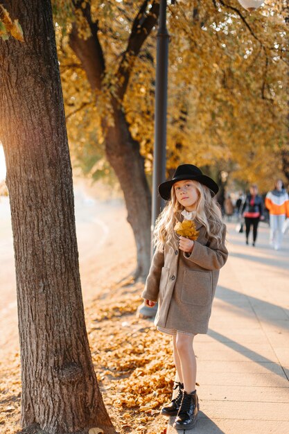 暑い晴れた秋の日に帽子をかぶった幸せな白髪の少女がウォーターフロントを歩く