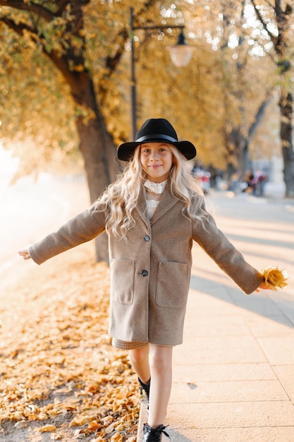 Happy whitehaired girl in a hat walks on the waterfront on a hot sunny autumn day