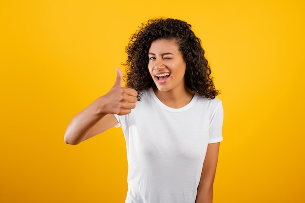 Happy winking black african woman isolated over yellow