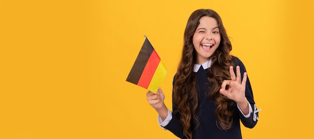 Happy winking child hold german flag yellow background showing ok gesture education abroad