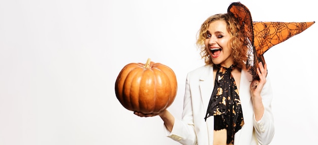 Foto ragazza ammiccante felice in cappello della strega con la donna sorridente del partito di halloween della zucca con jackolantern