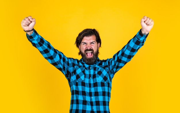 Happy winner handsome man gesturing and keeping mouth open while standing against yellow background happiness