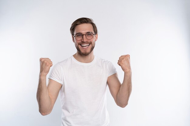 幸せな勝者。白い背景に立っている間、身振りで示すと口を開いたままにして幸せな若いハンサムな男。