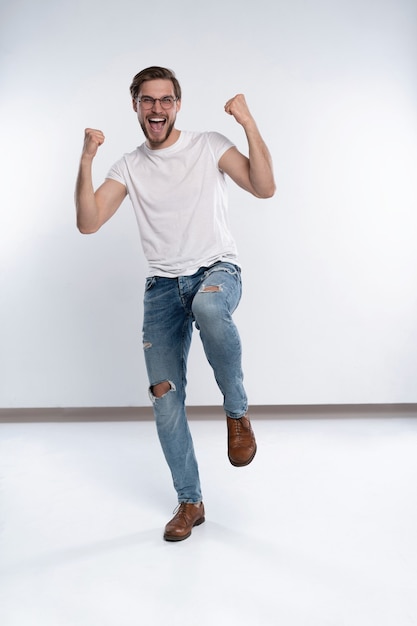 Happy winner. Happy young handsome man gesturing and keeping mouth open while standing against white background.