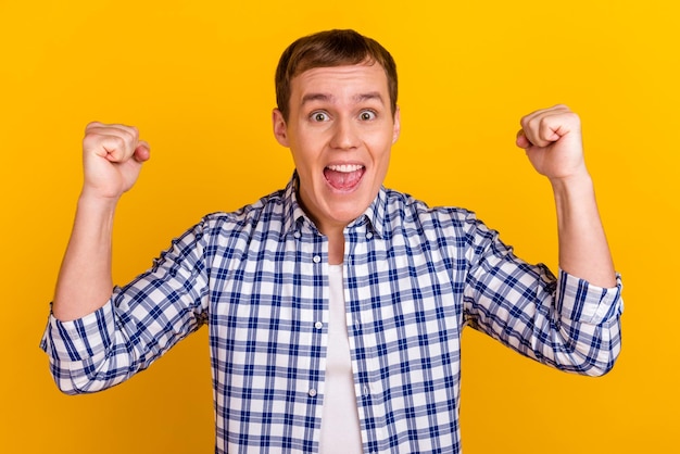 Happy winner Young handsome man gesturing fist up while standing against yellow vivid background celebrate championship