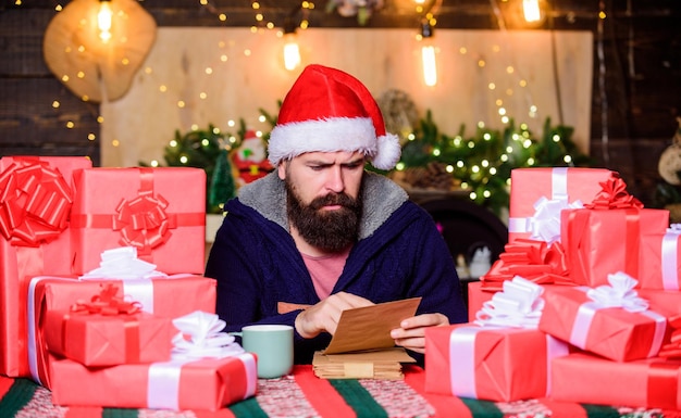 행복한 겨울 휴가 리본과 리본으로 포장 된 선물 Hipster는 가족을 위해 선물을 준비했습니다. 소중한 꿈을 이루십시오 남자 수염 난 산타 클로스 모자 독서 편지 관대 한 새해 많은 선물