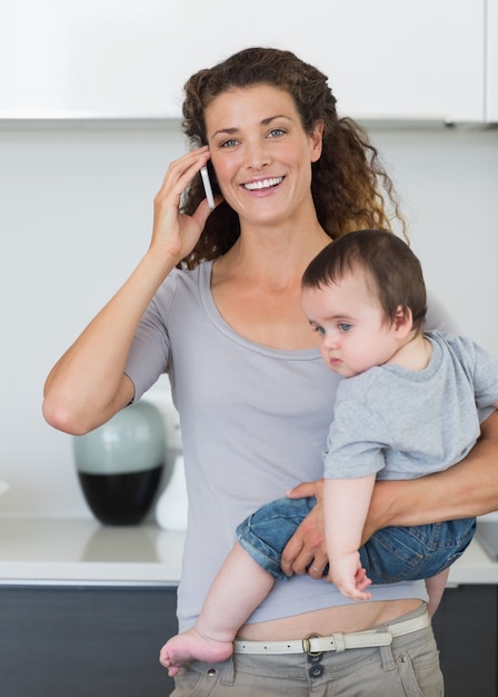 Happy woman answering smartphone while carrying baby