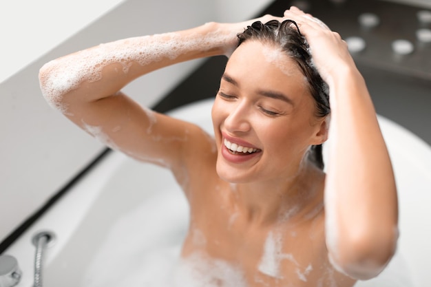Foto donna felice che applica shampoo testa di lavaggio facendo il bagno nel bagno