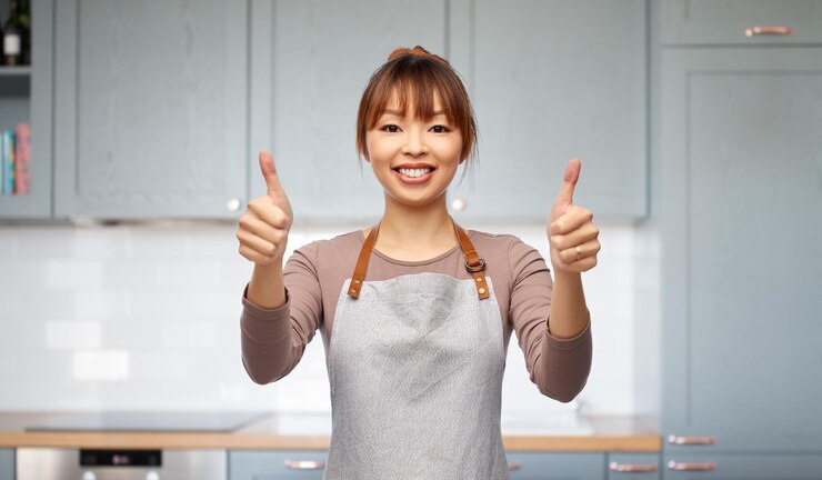 Photo キッチンで親指を挙げているエプロンを着た幸せな女性