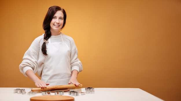 Happy woman baker in a white apron prepares new years cookies on a yellow background