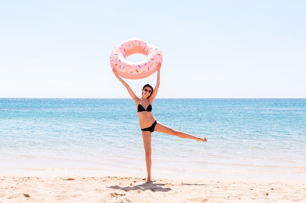 Donna felice sulla spiaggia che gioca con un anello di ciambella gonfiabile. vacanze estive e concetto di vacanza.