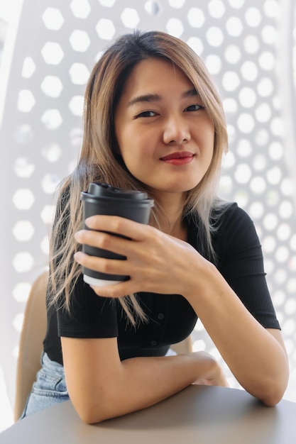 Photo happy woman in black tshirt sipping hot coffee in white coffee shop