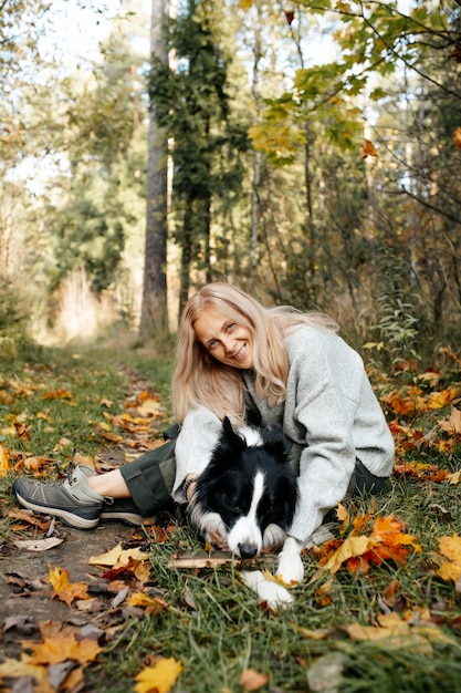 Happy woman and black and white border collie dog in autumn forest